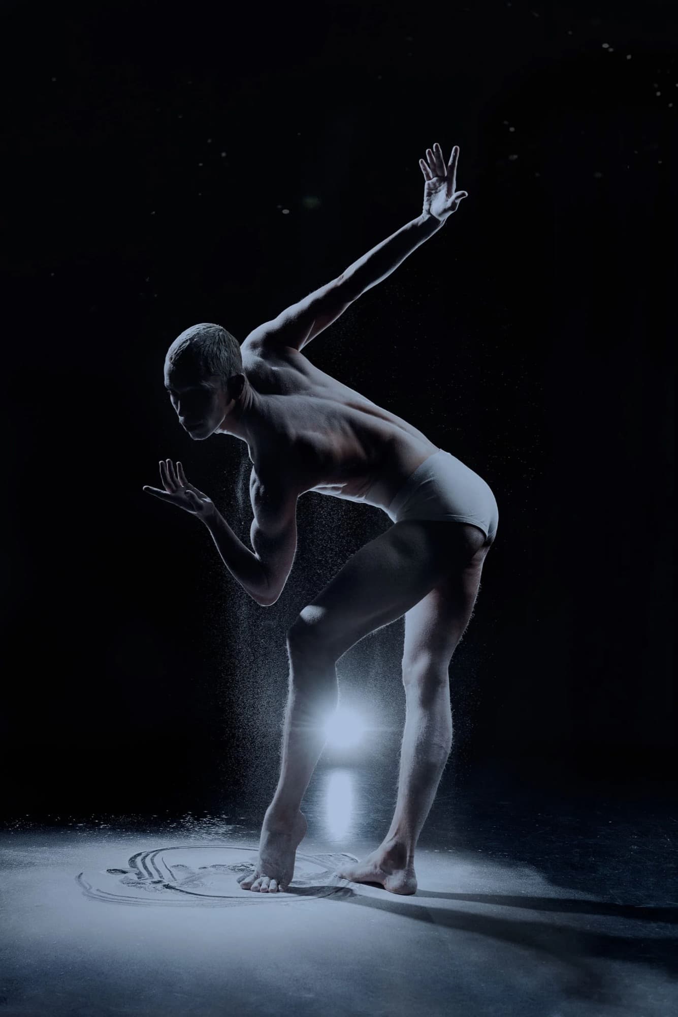 A dancer moving through light and powder in darkness